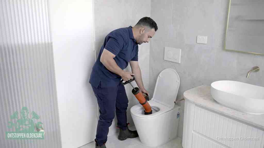 Een monteur buigt over een wandcloset en duwt met de hand een persluchtontstopper in de toiletpot om de verstopping handmatig los te maken in Oldenzaal
