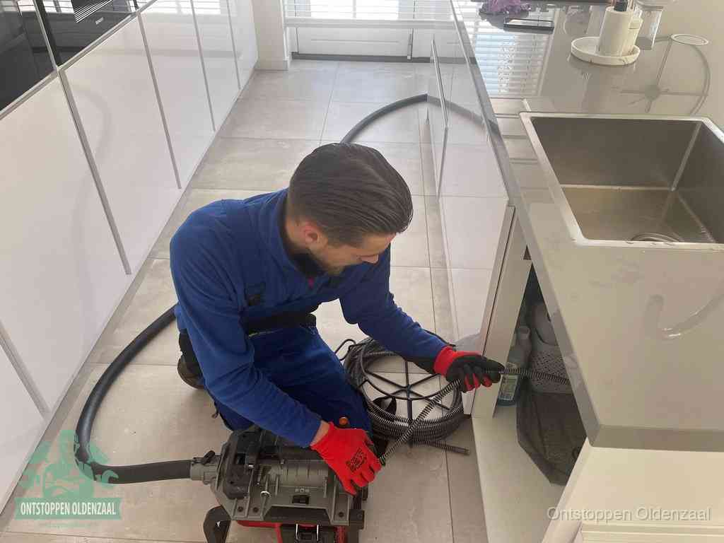 Een monteur ontstopt de keukenafvoer onder de spoelbak met een elektrische veermachine in Oldenzaal