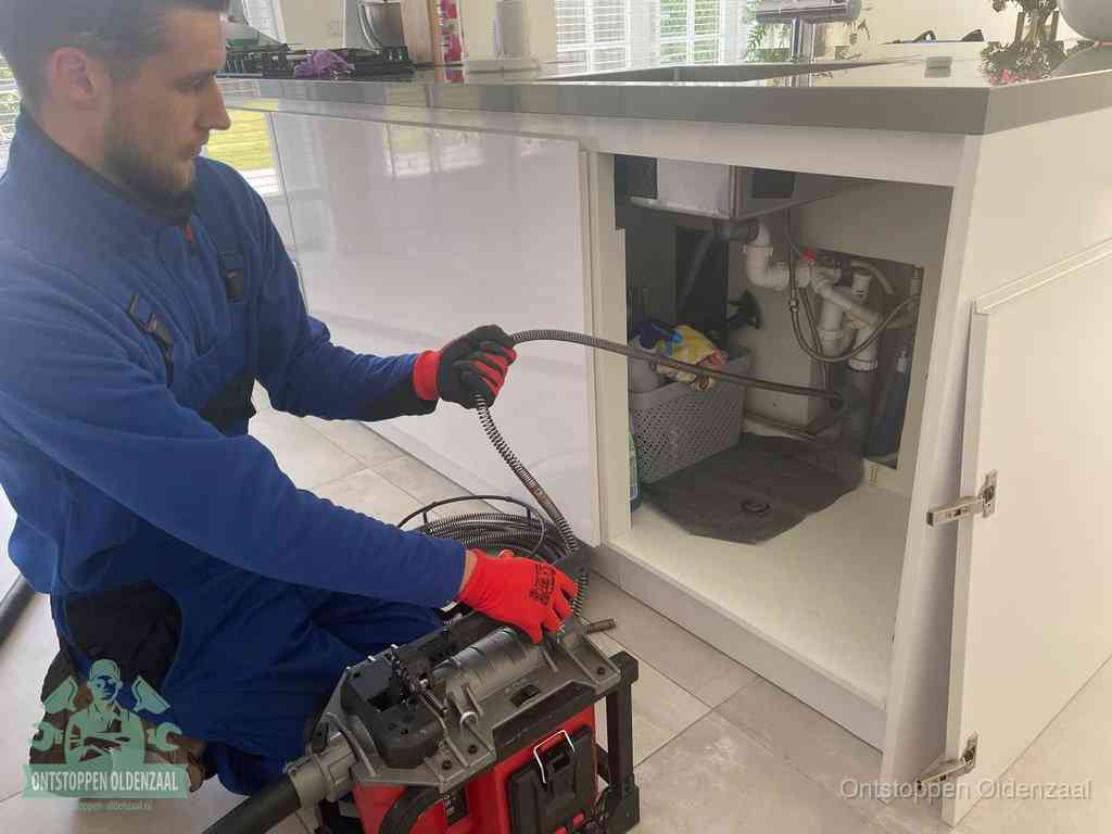 Monteur voert een ontstoppingsveer in de afvoer onder de keuken in Oldenzaal