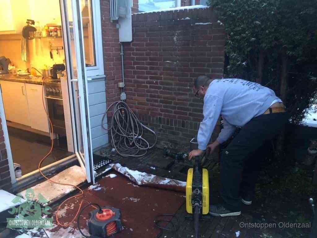 Een monteur werkt buiten bij een open riool-/grondput met een elektrische ontstoppingsmachine om een verborgen afvoerprobleem op te sporen in Oldenzaal