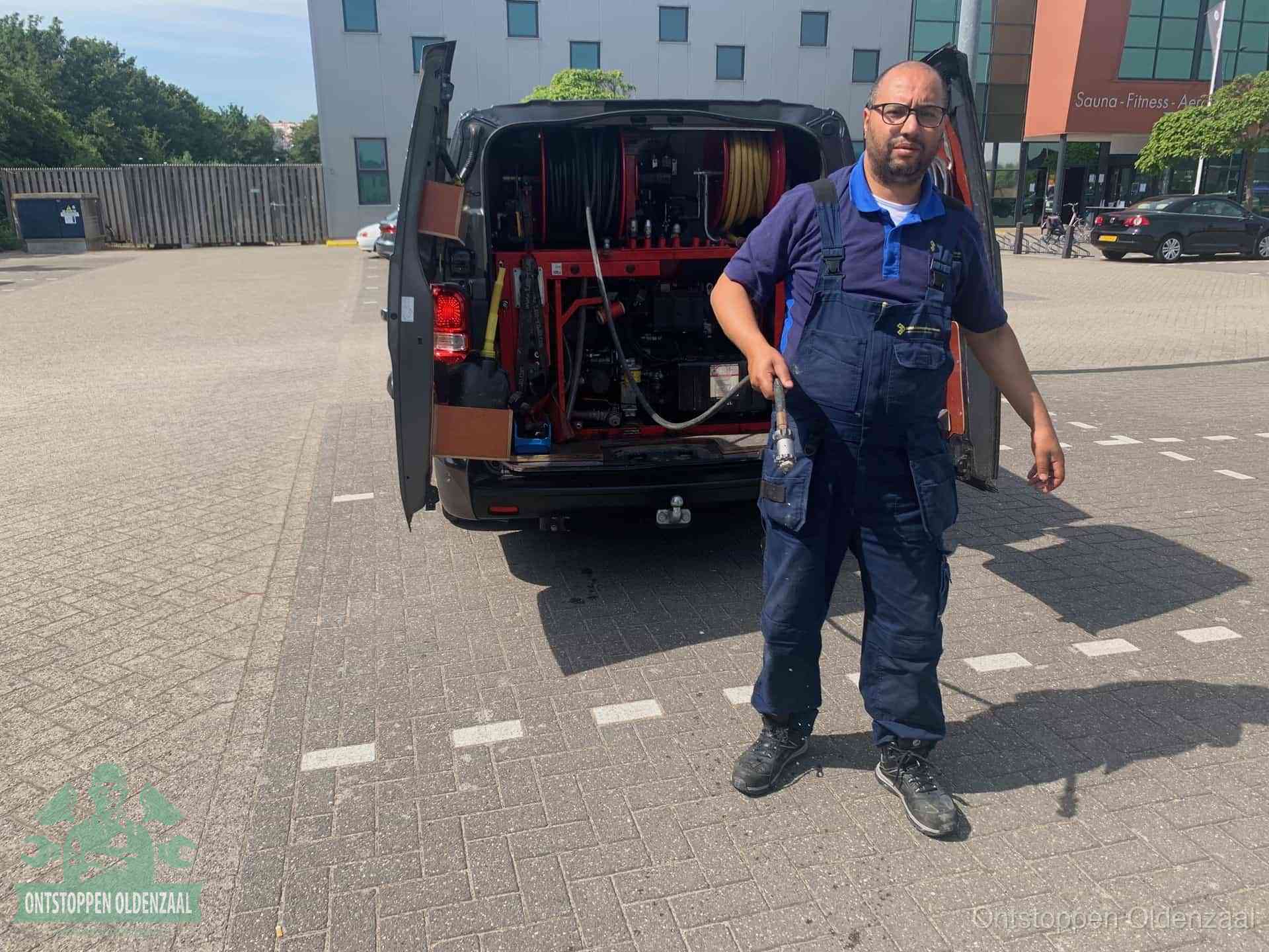 Een monteur bij zijn bestelbus met een hogedruk- en rioolreinigingsunit, klaar om de oorzaak van terugkerende wc-verstoppingen aan te pakken in Oldenzaal