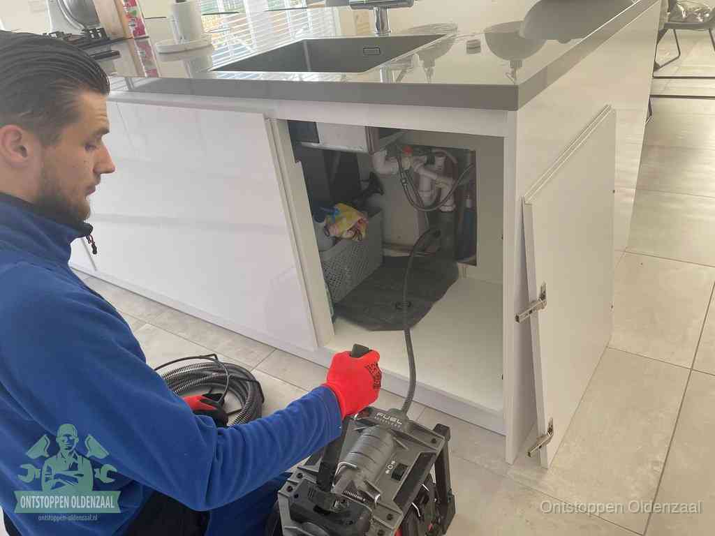Monteur ontstopt met een veermachine een verstopte afvoer onder de gootsteen in Oldenzaal
