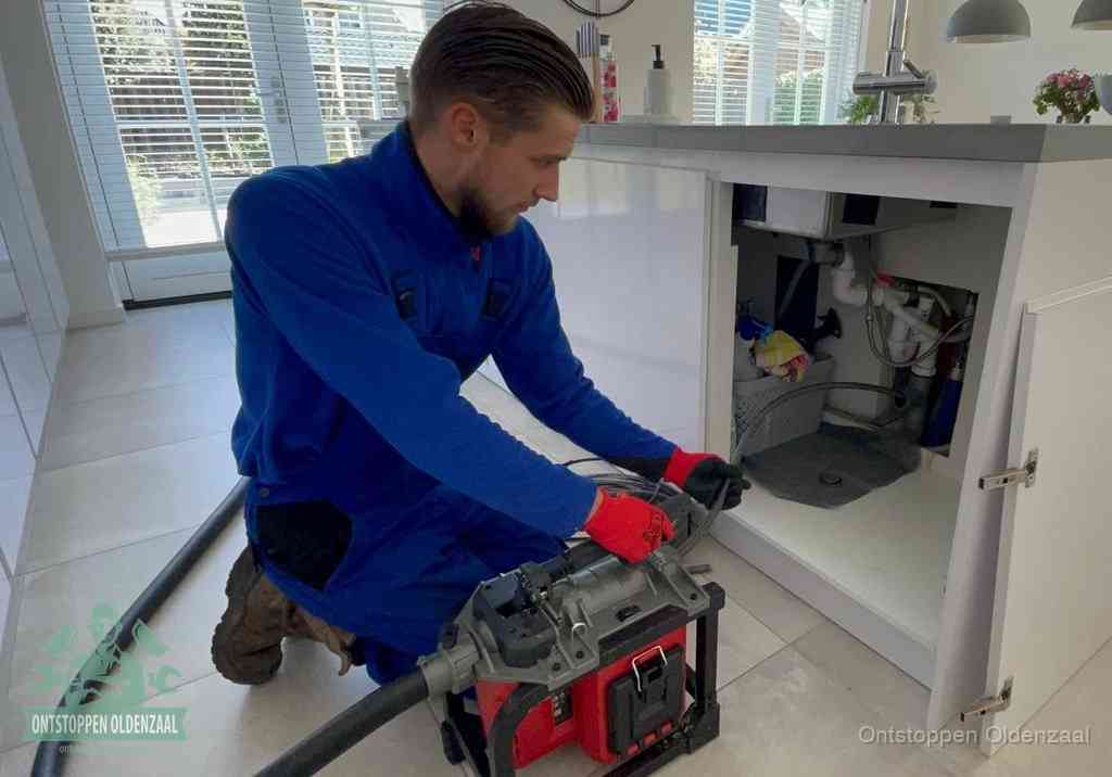 Een monteur voert een professionele elektrische ontstoppingsmachine in de afvoer onder de spoelbak tijdens het gootsteen ontstoppen in Oldenzaal